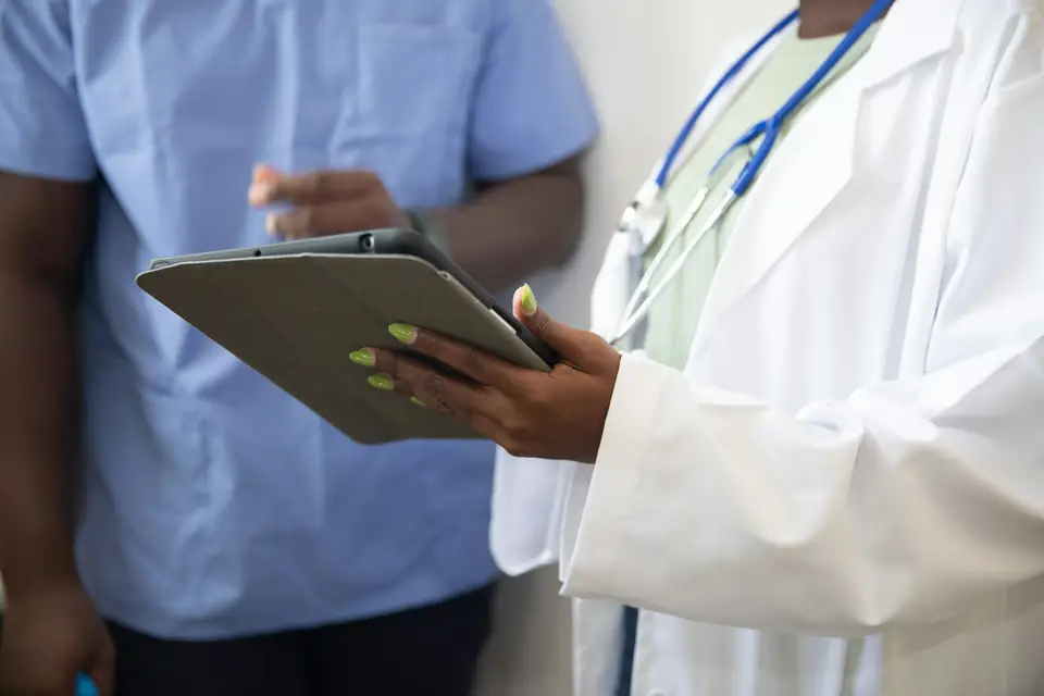 Médica de jaleco branco consultando um tablet ao lado de um enfermeiro
